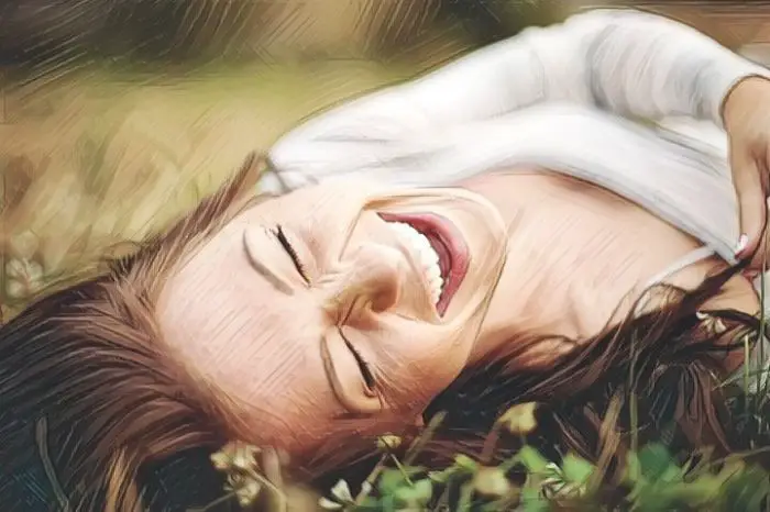 Una mujer tirada en el parque riendo a carcajadas y aprovechando los beneficios de la risa