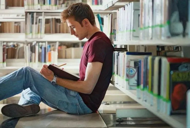 Persona joven introvertida en la biblioteca leyendo un libro